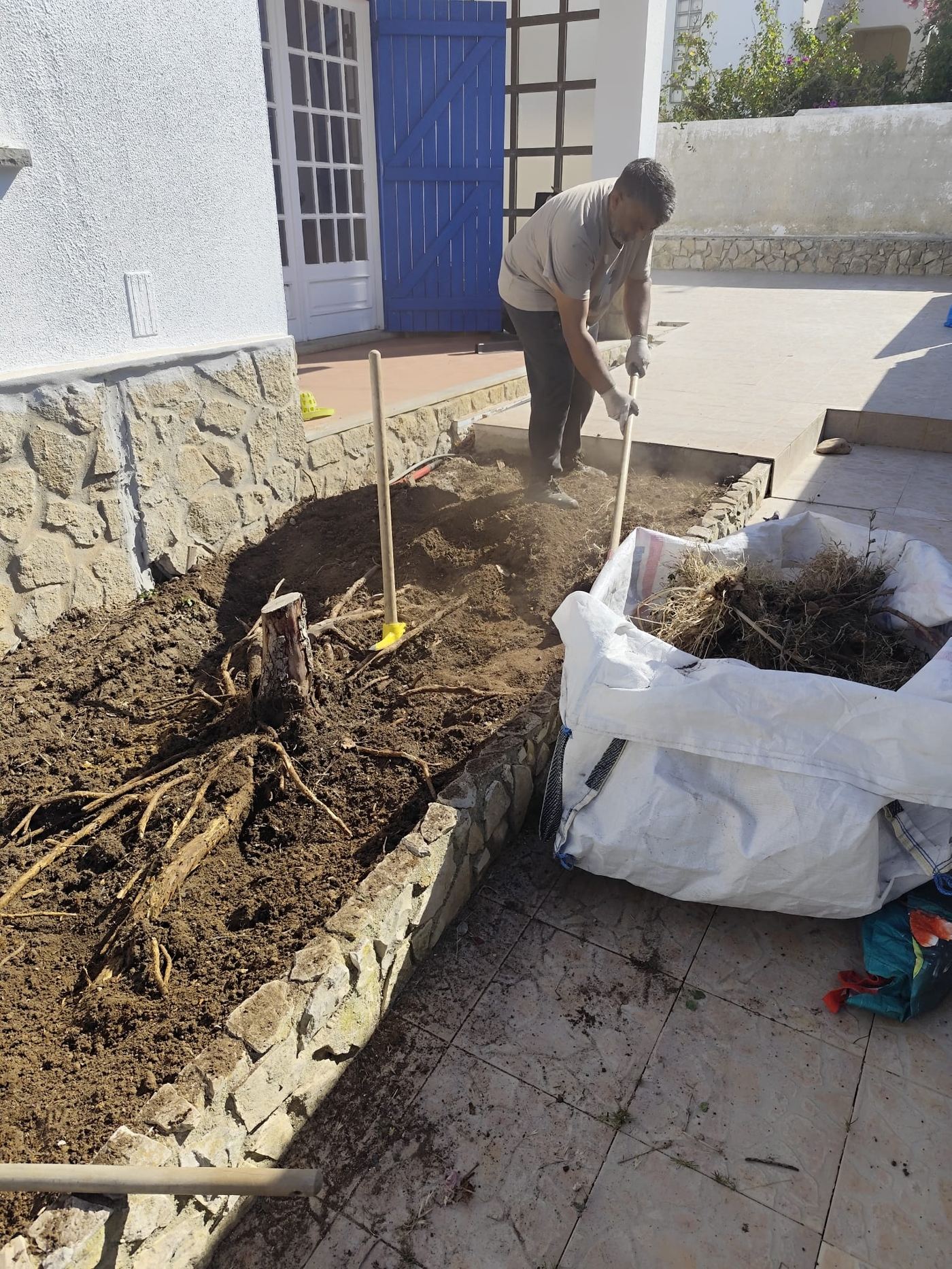 Trabalhador a remover raízes de um canteiro junto à casa