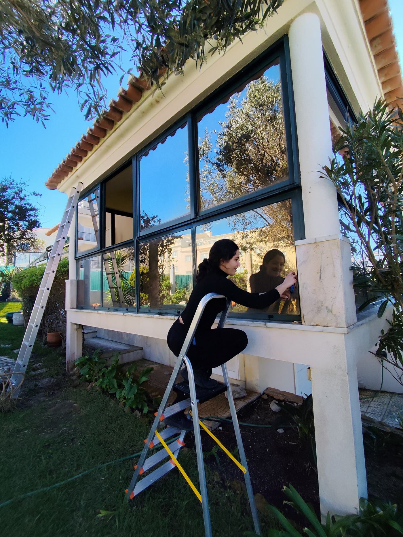 Trabalhadora a tratar a vedação de uma janela exterior em escadote