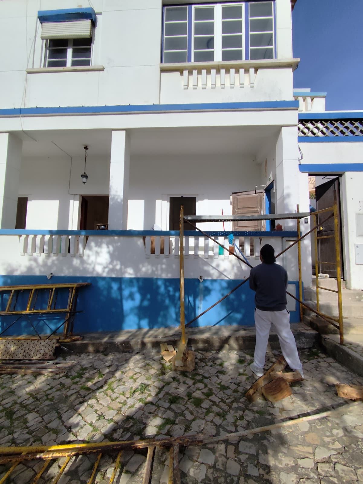 Trabalhador a pintar a fachada azul e branca de uma moradia