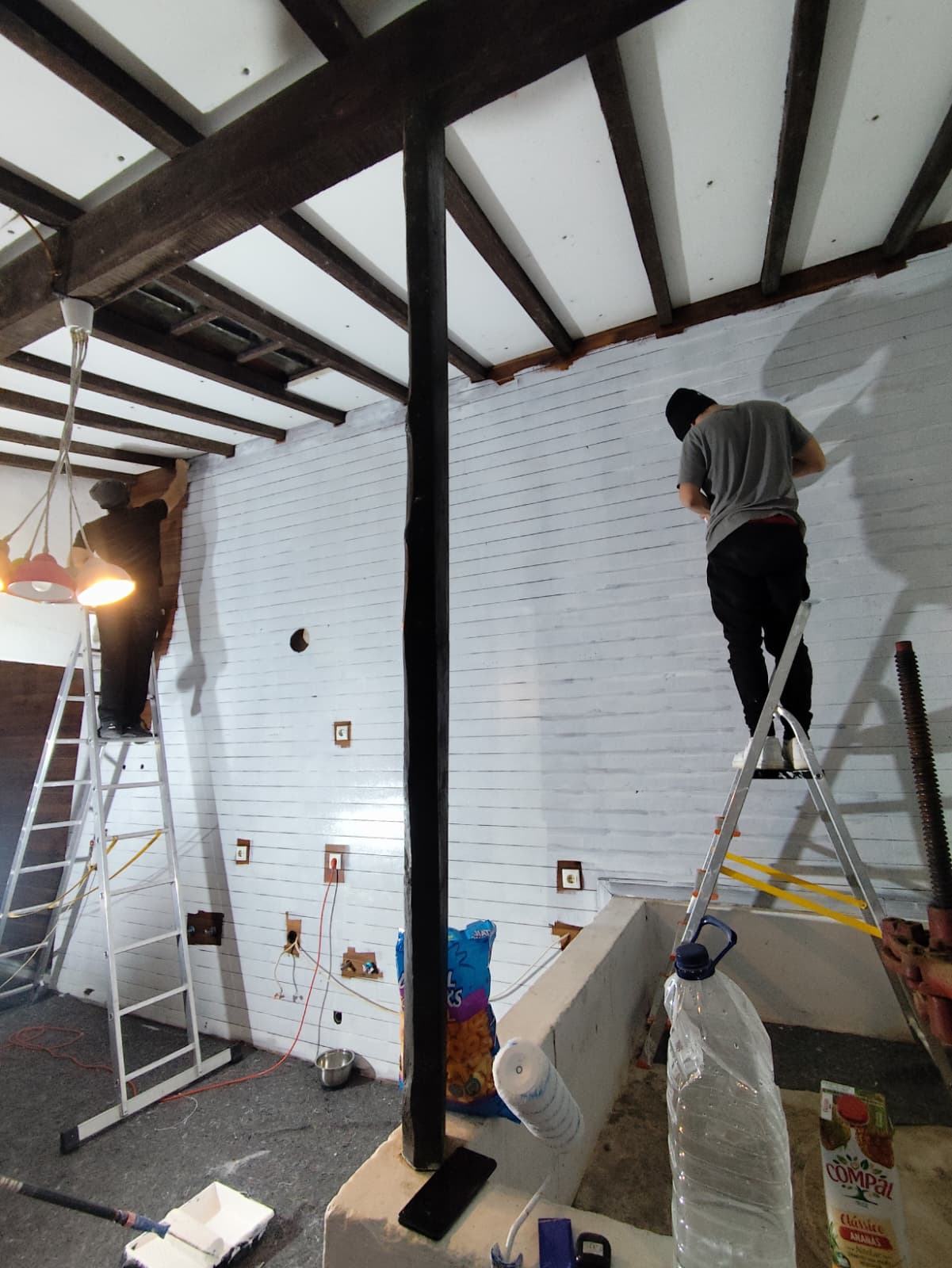 Dois trabalhadores em escadotes a pintar a parede em madeira de branco
