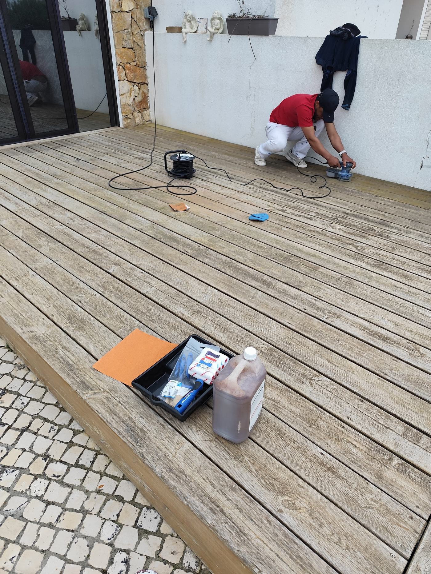 Trabalhador a lixar deck de madeira com lixadeira elétrica