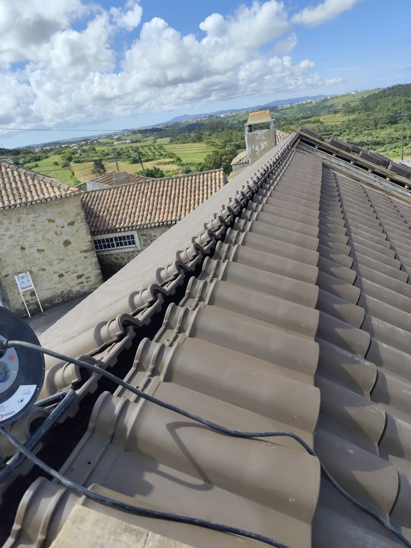 Cumeeira do telhado com telha nova instalada, vista sobre o campo