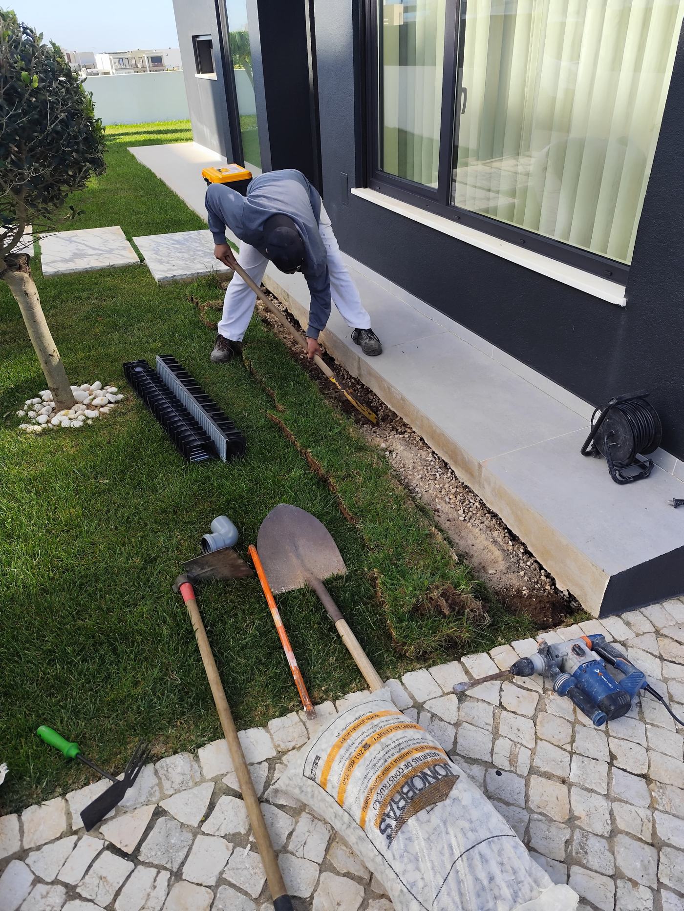 Trabalhador a abrir vala junto à fachada para colocação de dreno